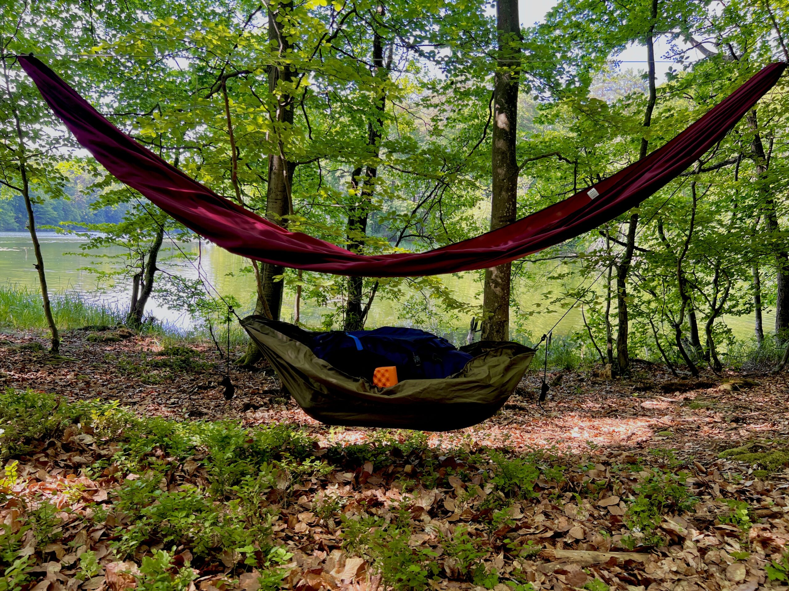 Bagażówka wisząca pod hamakiem. Zdjęcie przedstawia hamak hikari w leśnej scenerii z rozwieszoną pod nim bagażówkę. W mini hamaku schronienie znalazł plecak.. Produkt marki WYDRA 13.
